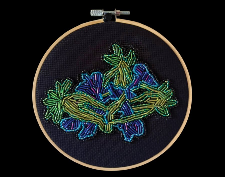 Beaded embroidery in an embroidery hoop: green and blue bugle beads form a branching multipolar spindle on dark fabric