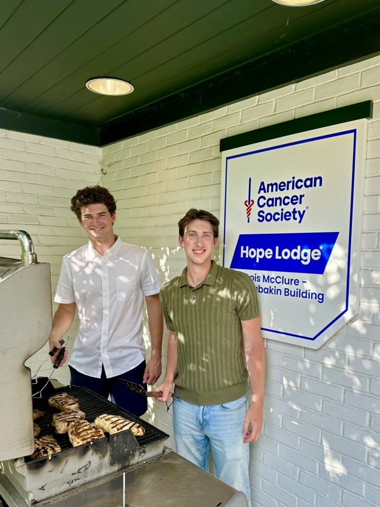 Two lab members grilling chicken beside the Hope Lodge sign